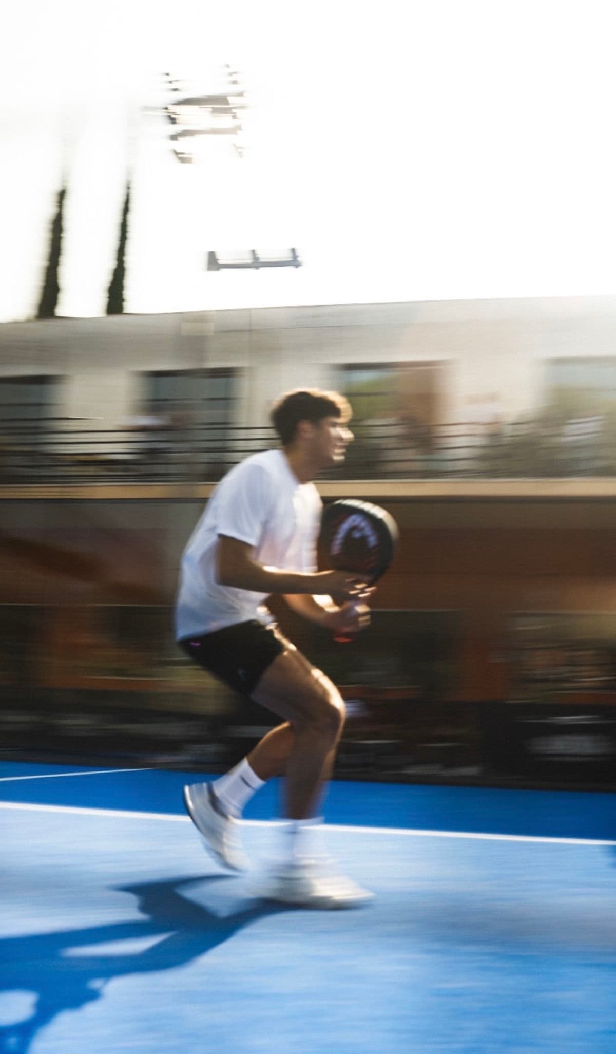 An athlete low and ready on a blue court, paddle in hand, caught in motion blur