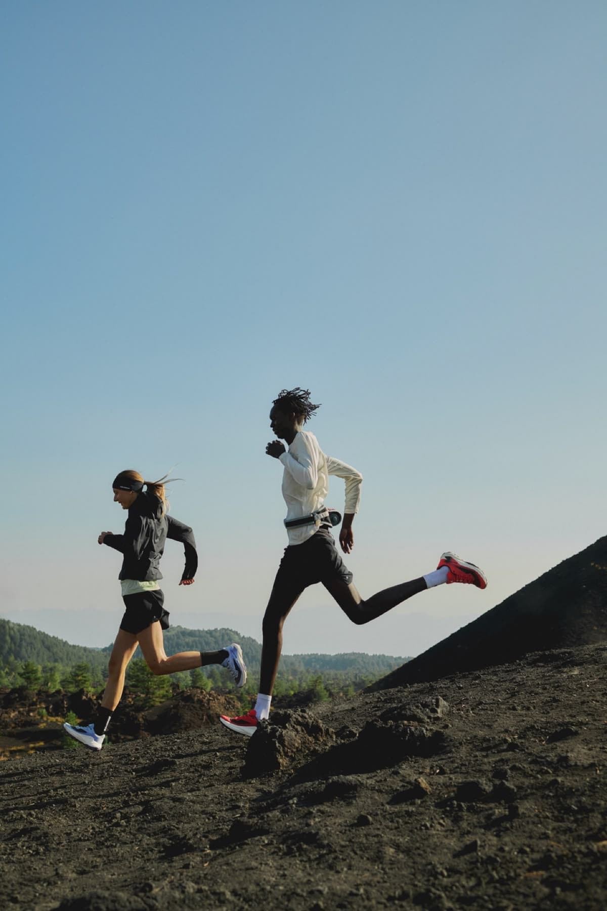 Two runners striding up a volcanic trail against an open sky